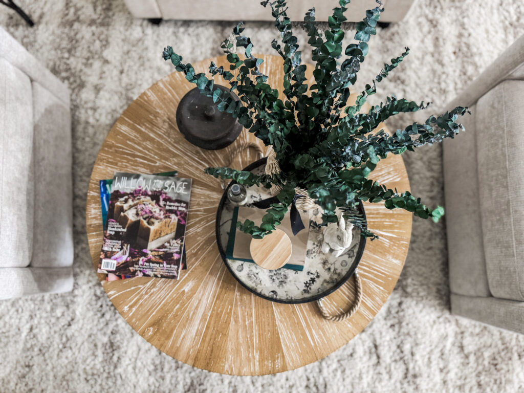 A cozy living room setup featuring a round wooden coffee table with a potted plant, candles, and magazines, creating a warm and inviting atmosphere for home decor enthusiasts.