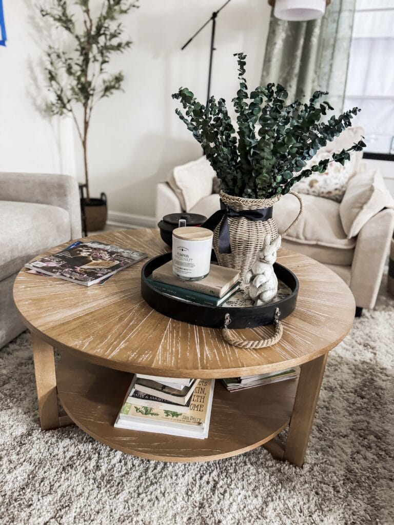 A cozy living room featuring a round wooden coffee table with a large potted green plant, candles, and magazines, creating a warm and inviting atmosphere perfect for relaxation and home decor.