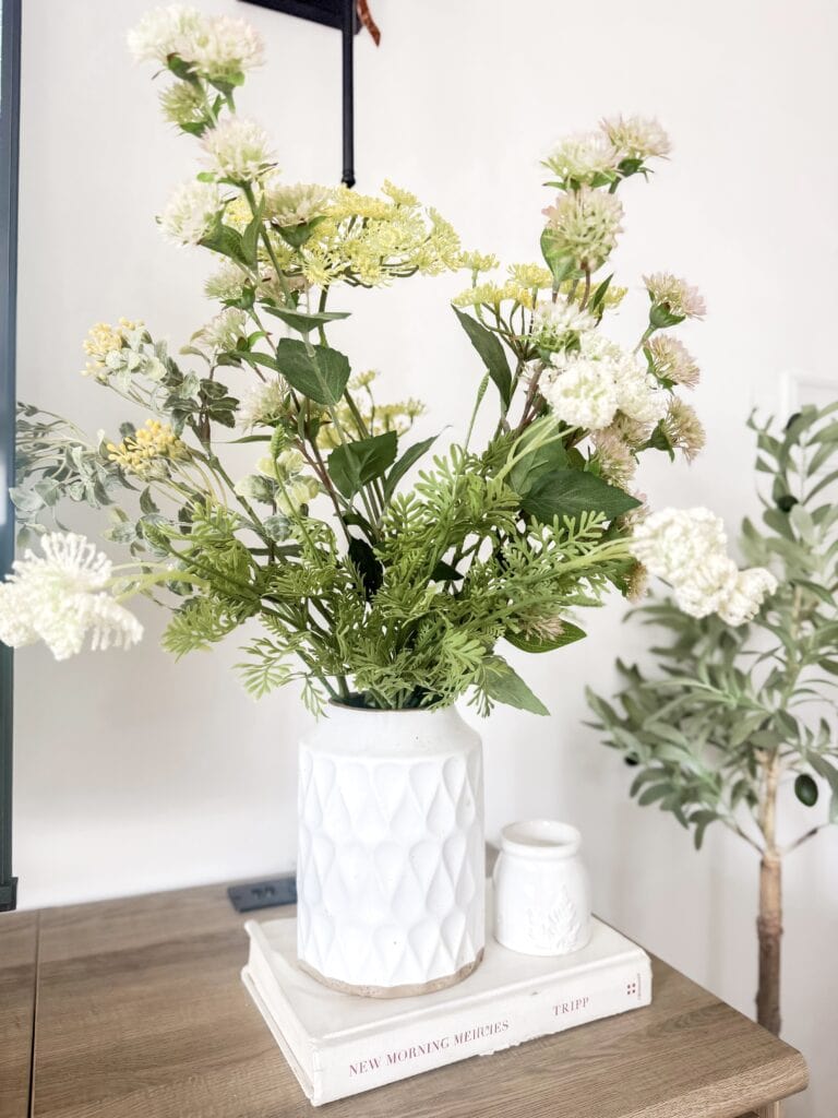 A beautiful white flower bouquet featuring carnations and greenery in a textured white ceramic vase, styled for home decor and floral arrangements.