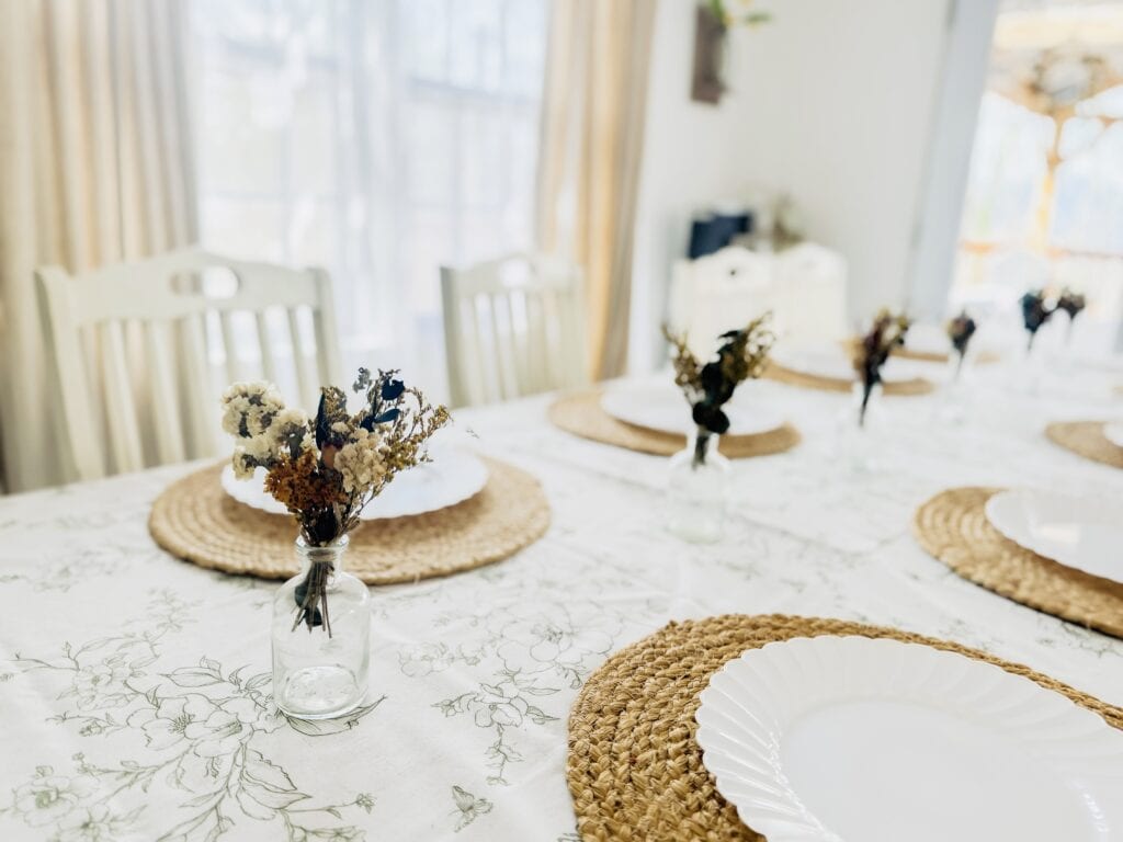 Beautifully set dining table with floral arrangements, woven placemats, and natural light, perfect for family gatherings or special occasions, showcasing cozy and stylish home decor.