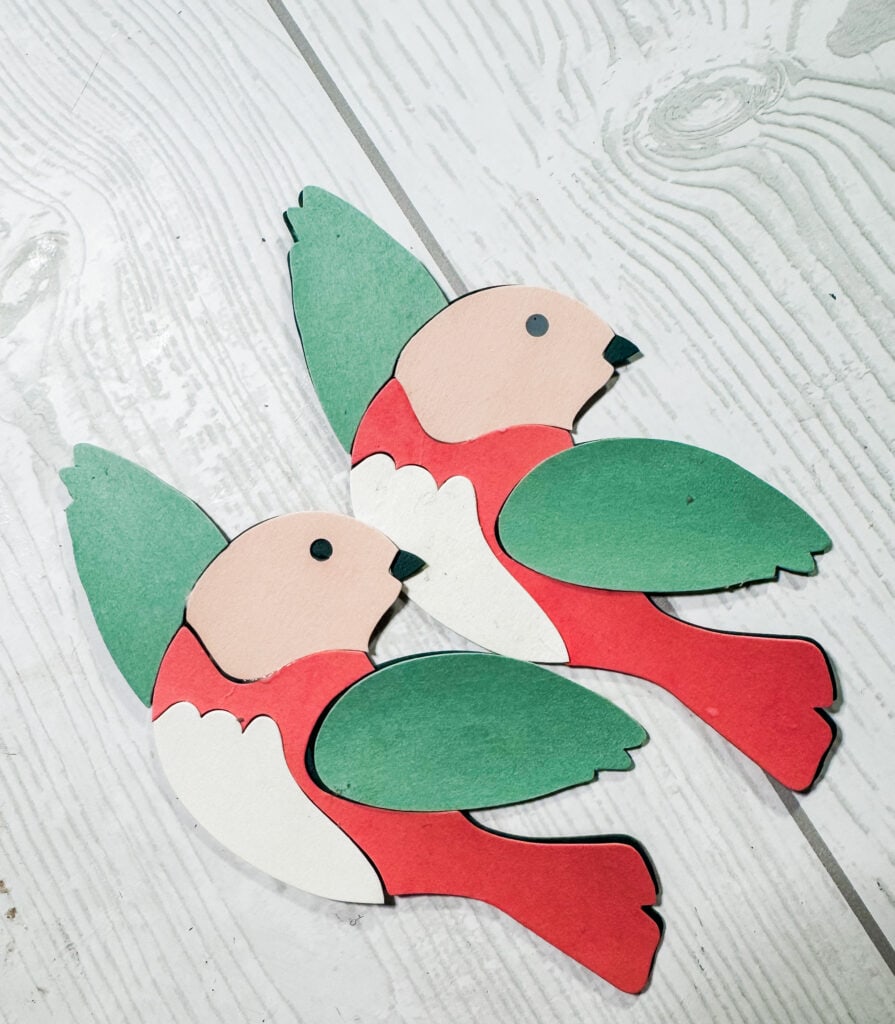 Colorful paper craft birds with red, green, and beige tones, perfect for holiday decor or craft projects, displayed on a light wooden surface.