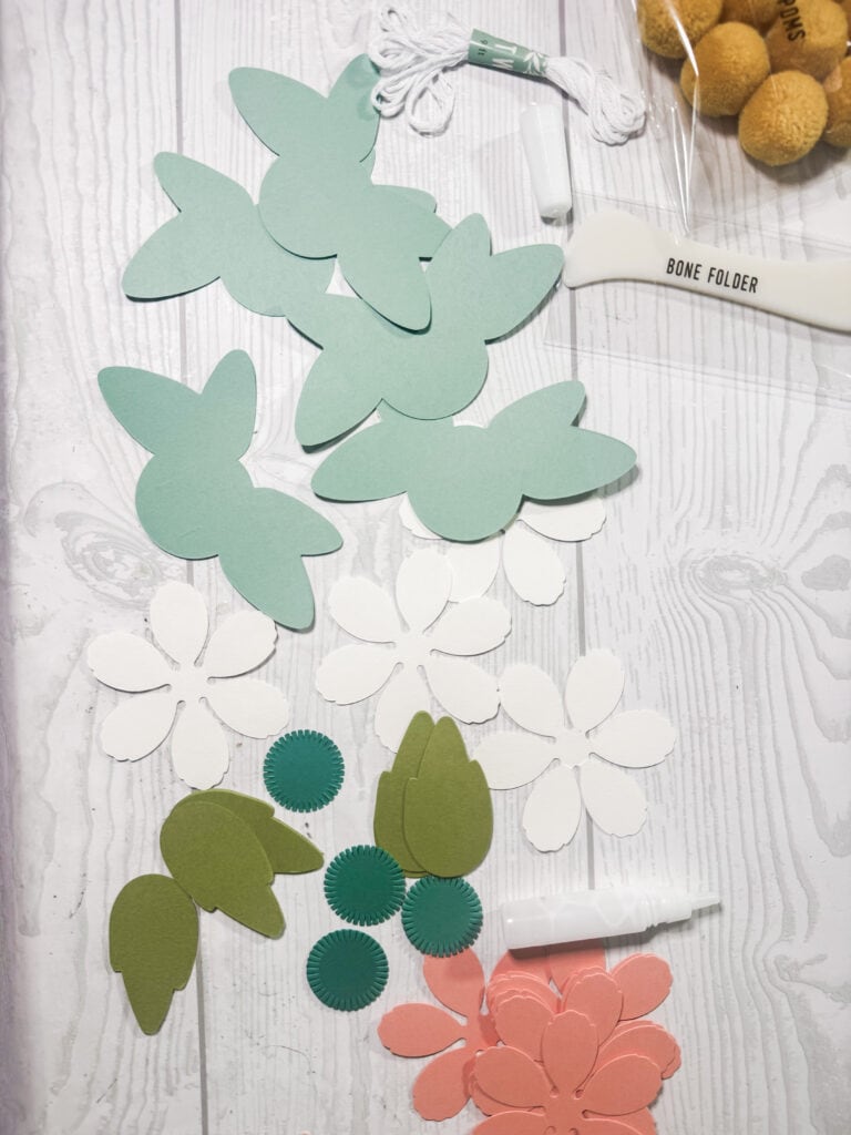 Colorful paper bunny and flower cutouts for DIY Easter and spring decor, featuring pastel green, white, and pink designs, along with crafting tools and embellishments.