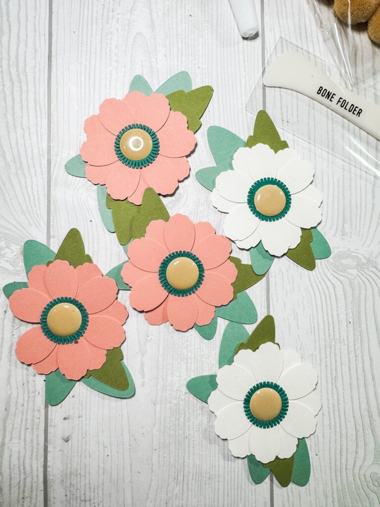 Colorful paper flower decorations with green leaves and beige centers, perfect for DIY home decor or craft projects.