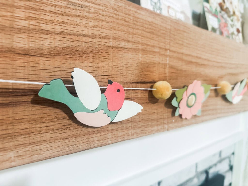 Colorful paper bird and flower garland decoration hanging on a wooden wall, ideal for home decor, parties, and spring celebrations. Bright, cheerful, and handcrafted aesthetic.