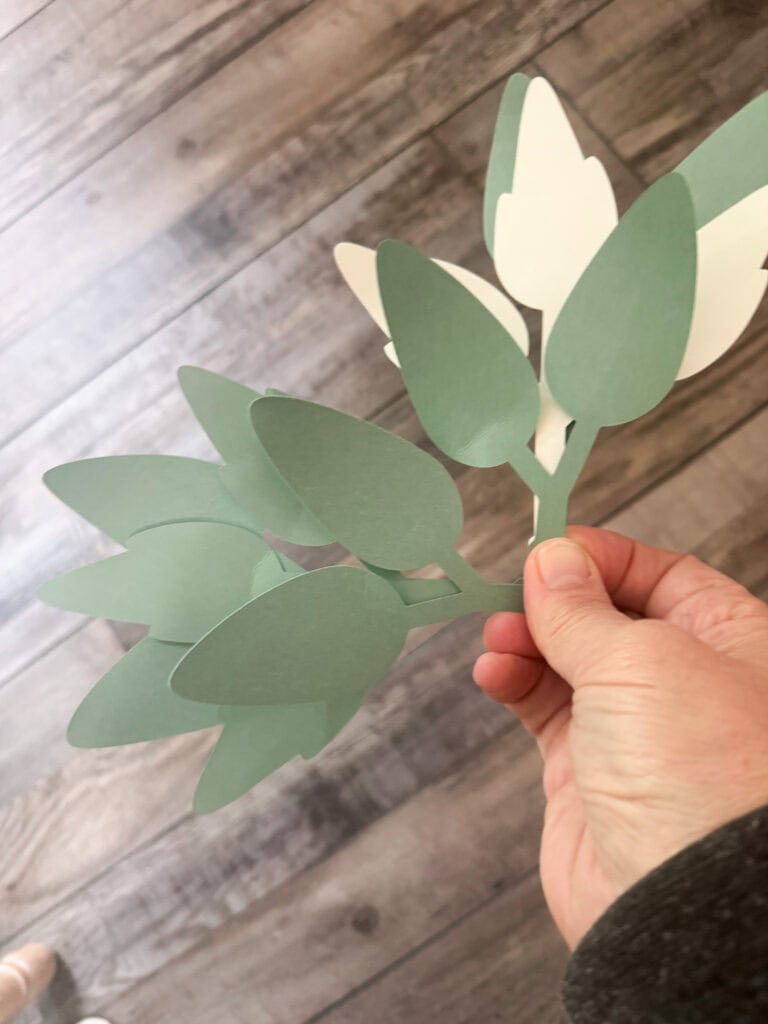 A paper craft featuring green and cream paper leaves held by a hand, showcasing a handmade botanical design perfect for home decor or craft projects.