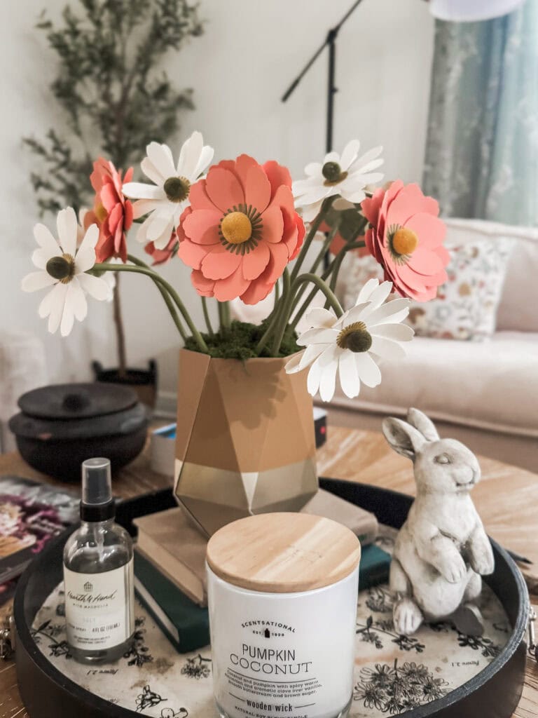 Aesthetic floral decor with pink and white flowers in a geometric vase, complemented by a cozy living room setting, decorative bunny, and scented candle for home ambiance.