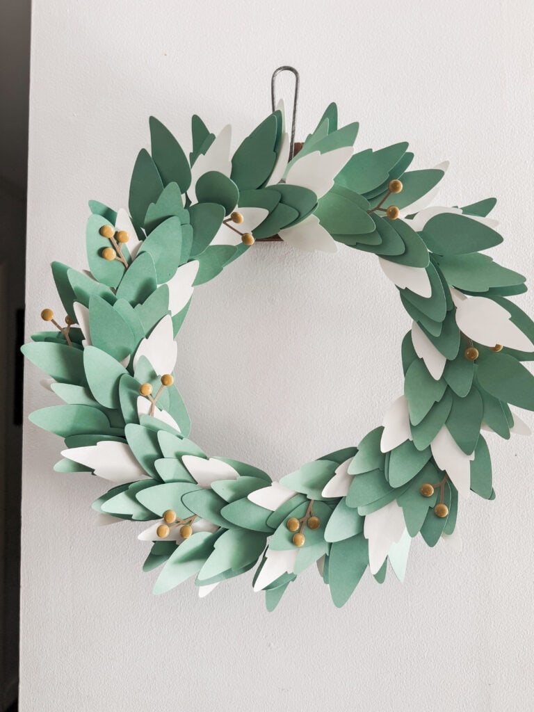 A beautiful handmade paper wreath featuring green leaves and gold accents, perfect for wall decor, seasonal decoration, or as a gift accessory.