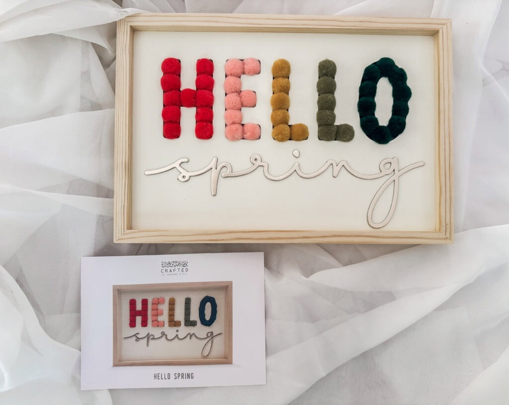 Decorative spring sign featuring the word "HELLO" in colorful felt letters and "spring" in cursive, set in a wooden frame for seasonal home decor.