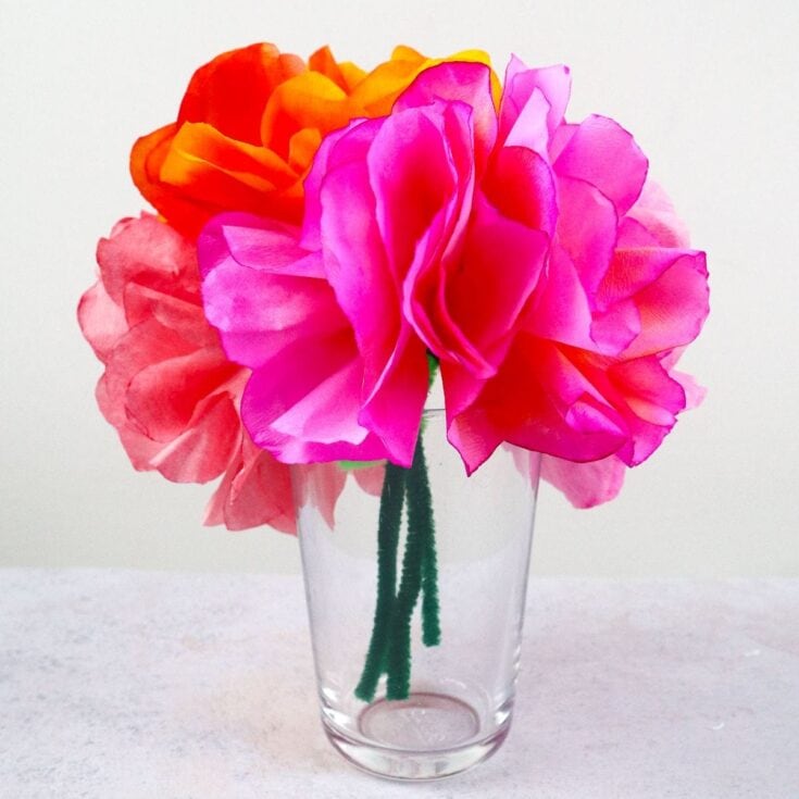 Vibrant paper flower bouquet with pink, orange, and red blooms in a clear glass vase, perfect for home decor or special occasions.