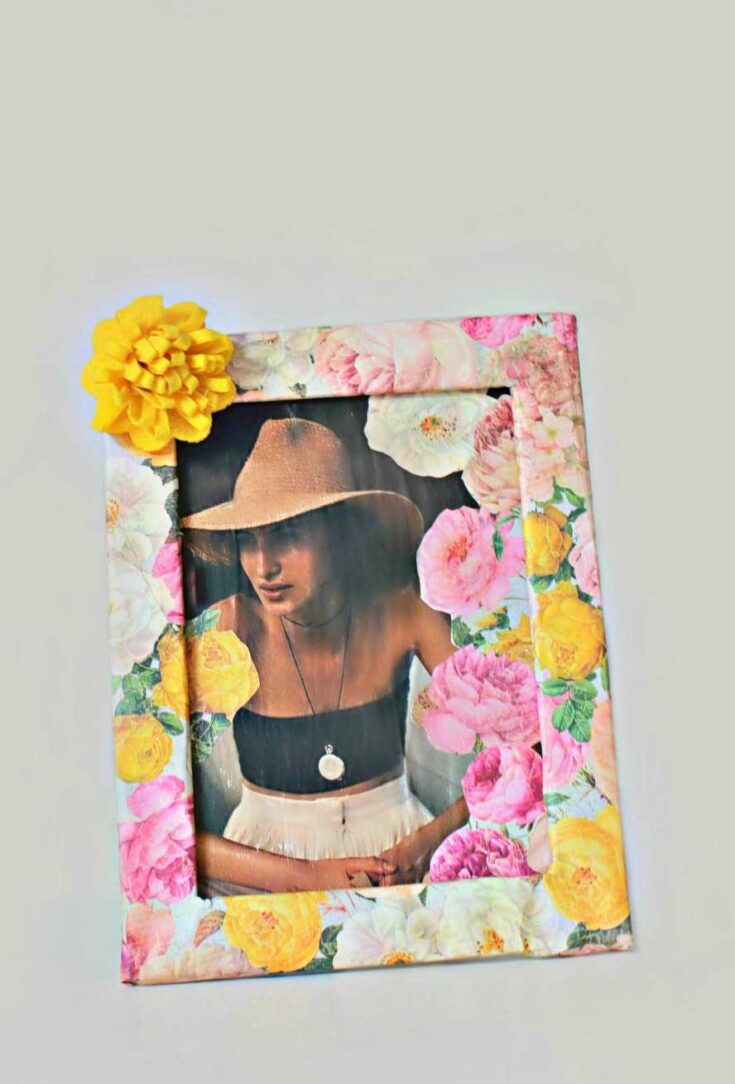 A woman wearing a wide-brimmed hat and black top, framed by a colorful floral border with pink, yellow, and white flowers, creating a vibrant and artistic portrait.