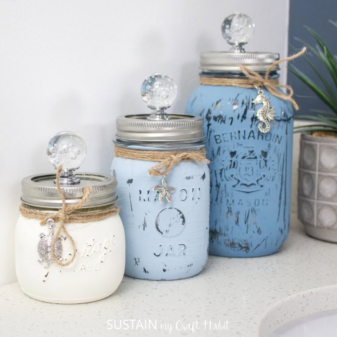 Decorative Mason jars with glass knobs, painted in soft pastel blue and white, featuring rustic twine accents, perfect for home decor or craft projects.