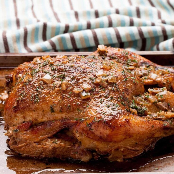 Juicy roasted chicken garnished with garlic, herbs, and a flavorful glaze, served on a rustic wooden surface for a hearty meal.