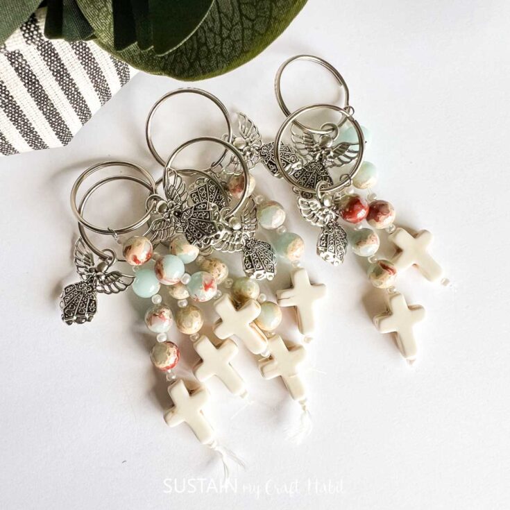 Elegant handmade earrings featuring white crosses, pastel beads, and silver leaf charms, perfect for religious or casual wear, displayed on a white background.