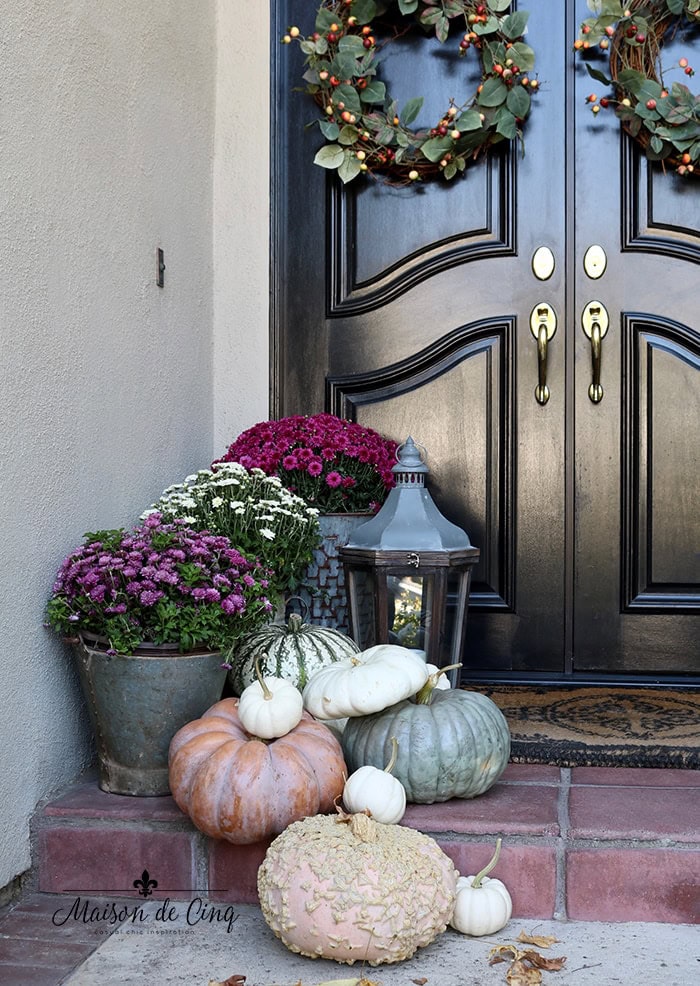 Autumn porch decor featuring pumpkins, mums, and wreaths on a black door, perfect for fall home decorating ideas.