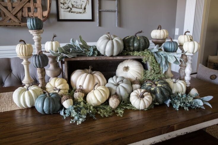 Fall pumpkin centerpiece with white, green, and blue pumpkins, surrounded by greenery and candles, perfect for seasonal home decor.