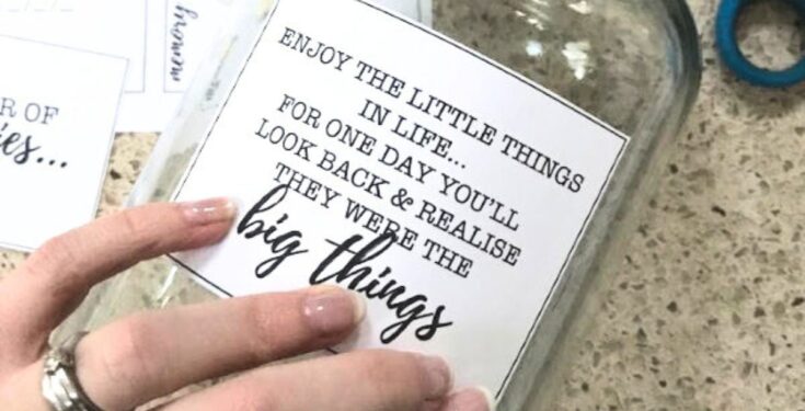 Close-up of a hand holding a glass jar with an inspirational quote about enjoying little things in life, perfect for home decor or motivational content.