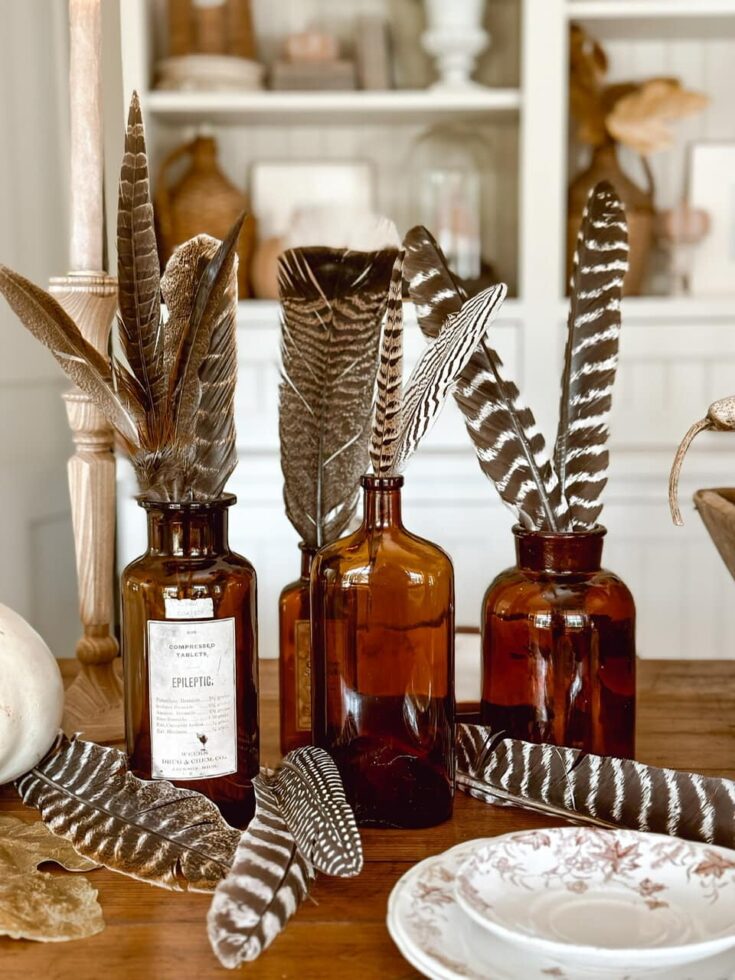 Decorative feathers in amber glass bottles create a stylish fall home decorating display, perfect for a cozy and sophisticated autumn ambiance.