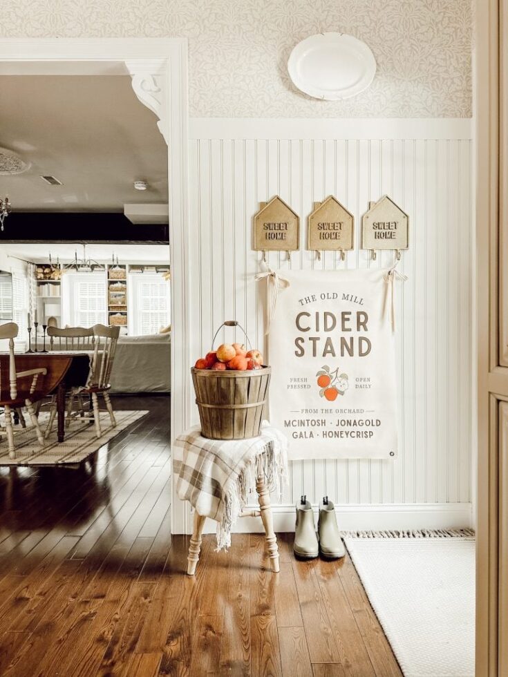 Cozy fall home decorating idea featuring a cider stand with apples, vintage signs, and rustic accents in a welcoming entryway.