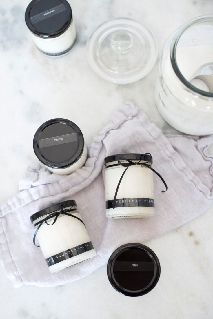 Elegant cream candles with black ribbons on a soft linen cloth, surrounded by glass jars of milk and a marble surface, perfect for cozy home decor or special occasions.