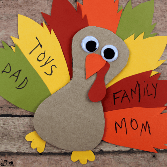 Colorful Thanksgiving turkey craft made with paper and googly eyes, featuring a brown body, orange beak, and vibrant paper feathers labeled with family roles like Dad, Mom, and Toys.