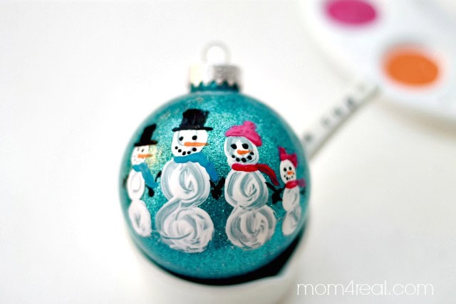 Decorative Christmas ornament featuring cheerful snowmen with scarves and hats, set against a glittery blue background, perfect for holiday decor and winter celebrations.