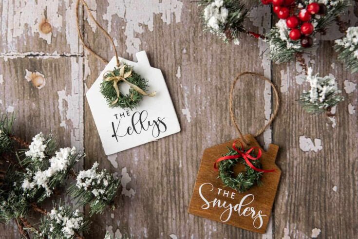 Decorative Christmas ornaments with personalized tags reading 'The Kellys' and 'The Snyders' on a rustic wooden background, surrounded by snow-dusted pine branches and red berries.