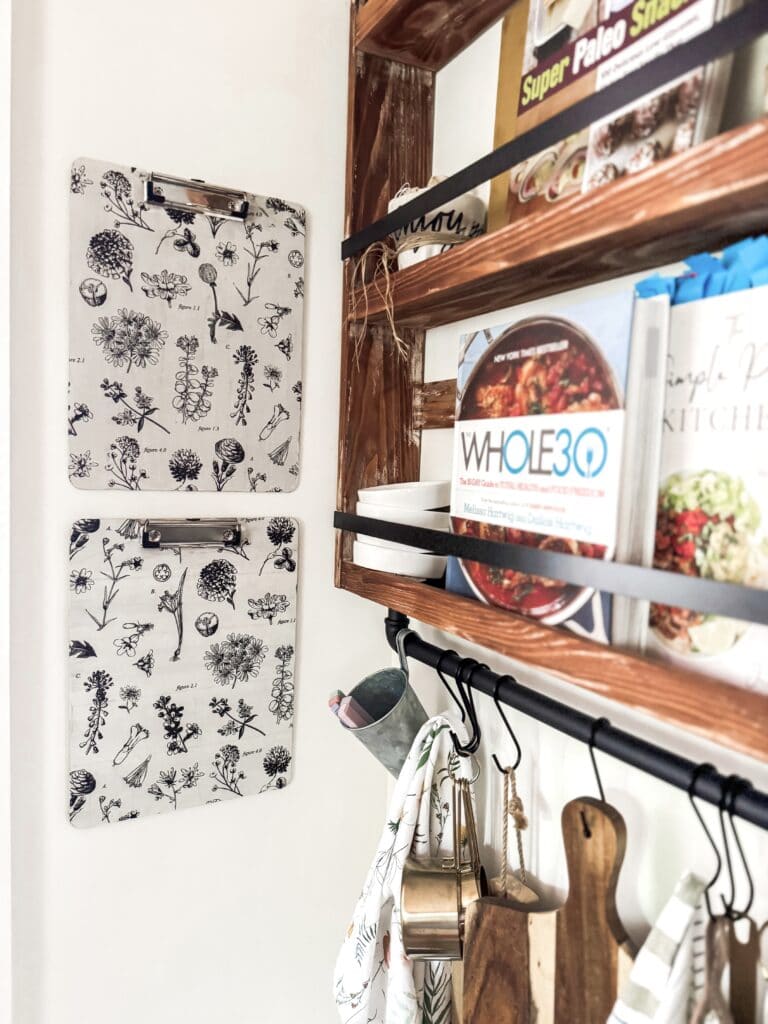Decorative kitchen wall with botanical prints and wooden shelves holding cookbooks and kitchen utensils, creating a cozy and stylish culinary space.
