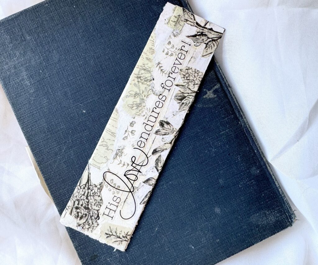 A blue hardcover journal with a decorative bookmark featuring a winter scene and the phrase "His Love endures forever" for inspirational writing and journaling.