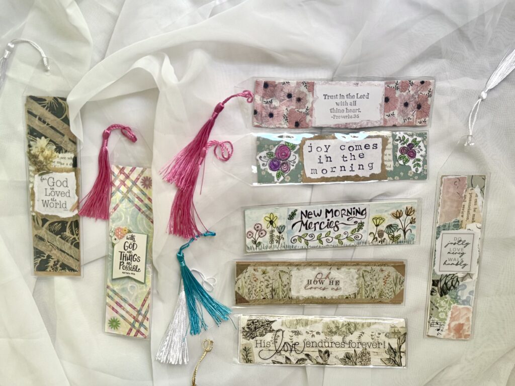 Set of six colorful bookmarks with inspirational quotes and tassels, perfect for journaling or gifting, displayed on a soft white fabric background.