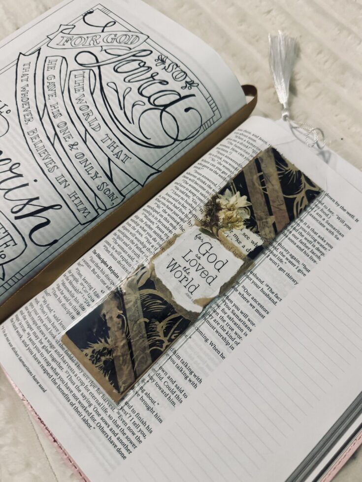Open Bible with a decorative bookmark reading 'God Loved the World' and hand-lettered inspirational art on the page, emphasizing faith and scripture.