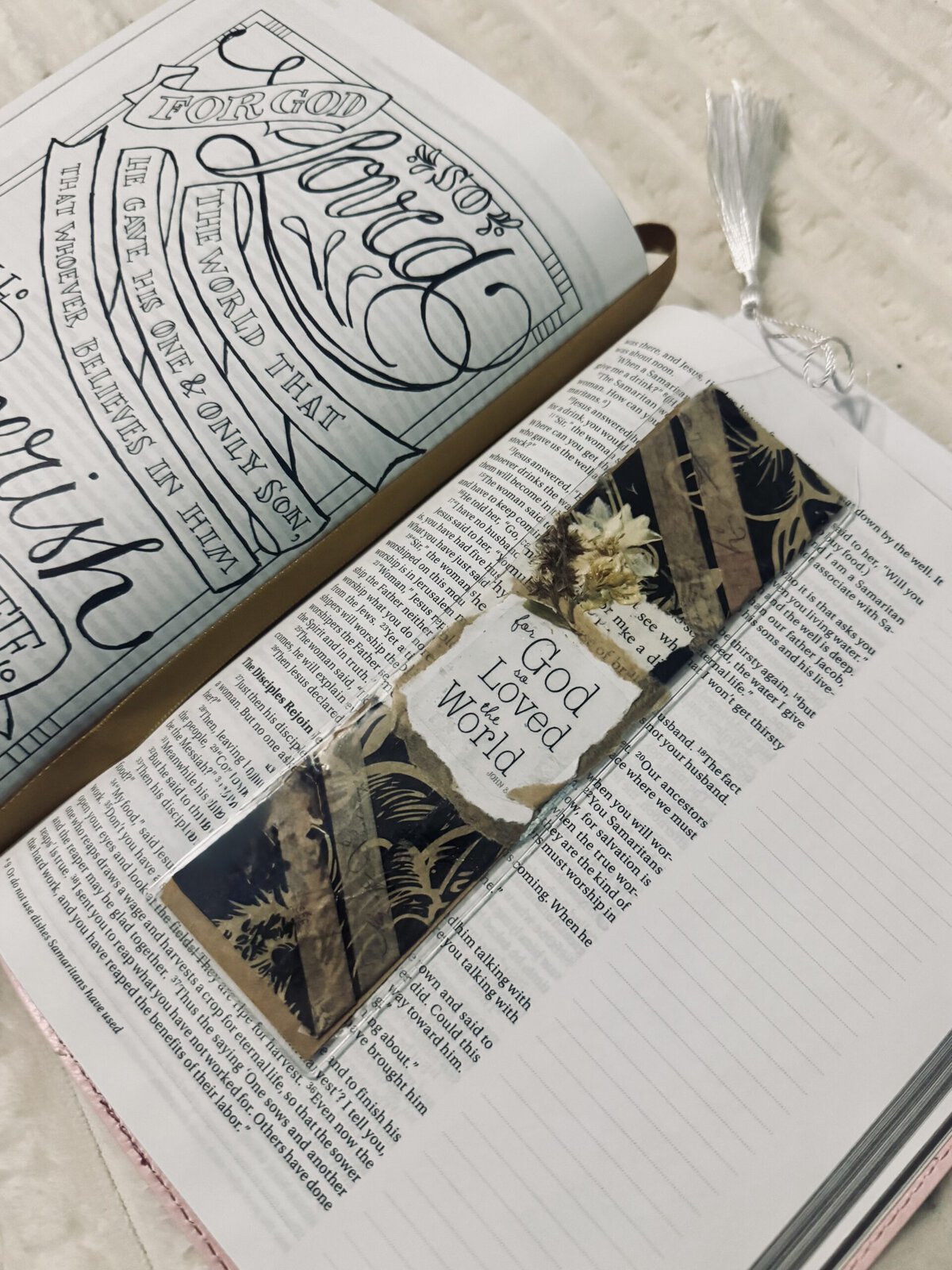 Open Bible with a decorative bookmark reading 'God Loved the World' and hand-lettered inspirational art on the page, emphasizing faith and scripture.