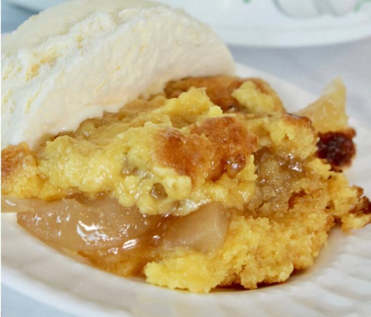 Close-up of a warm apple crisp with a golden crumb topping served with a scoop of vanilla ice cream on a white plate.