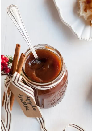 Close-up of a jar of homemade caramel sauce with cinnamon sticks and red berries, perfect for holiday desserts or gift-giving.
