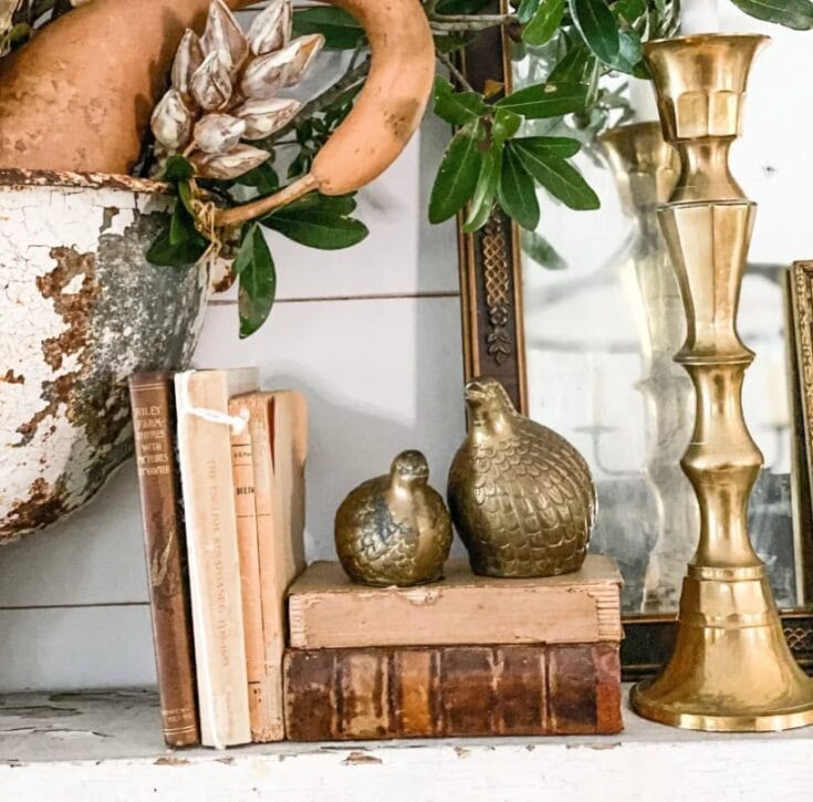 Decorative fall-themed home decor featuring gold vases, vintage books, and natural elements for a cozy autumn ambiance.