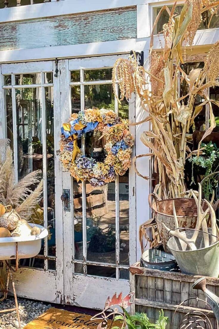Autumn home decorating ideas featuring a dried flower wreath on a rustic door, complemented by dried plants and seasonal accents for a cozy fall ambiance.