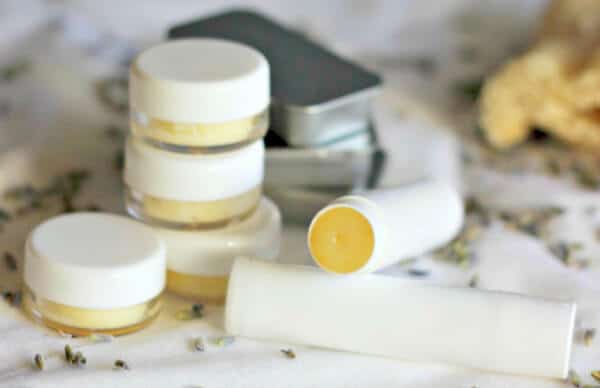 Collection of natural skincare creams and balms with a tube, jars, and a small black box, on a white surface with scattered herbs, promoting organic beauty and wellness.