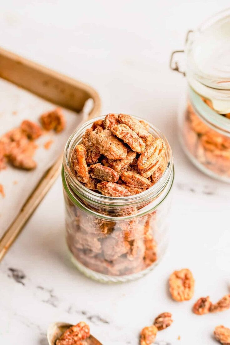 Close-up of homemade cinnamon sugar cookies layered in a glass jar, with a rustic background and additional cookies on a tray, perfect for gifting or snacking.