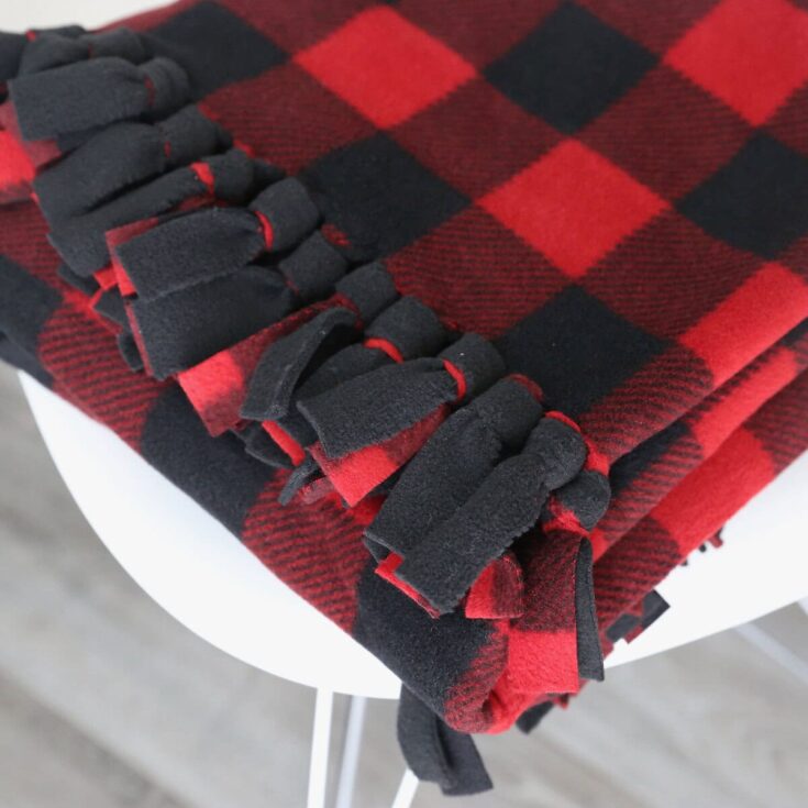 Close-up of a cozy red and black plaid blanket with fringe detail, perfect for adding warmth and style to your home decor.