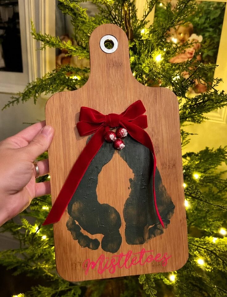 Wooden Halloween-themed cutting board with a black cat silhouette, red bow, and bells, hanging in front of a decorated Christmas tree for festive holiday decor.
