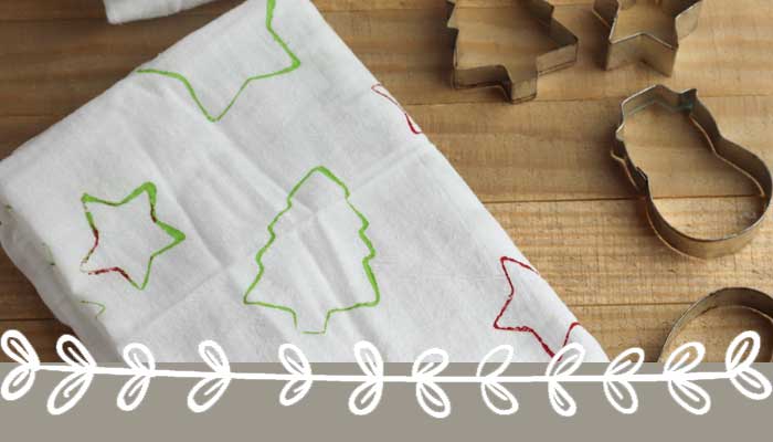 Christmas-themed cookie cutter shapes on a wooden surface with a festive cloth featuring star and tree outlines, perfect for holiday baking.