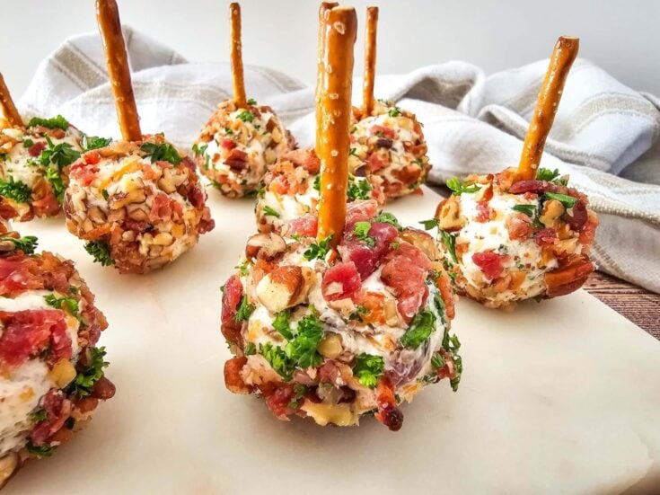Delicious meat and cheese appetizer bites with pretzel sticks, garnished with herbs, served on a white platter for a party or gathering.