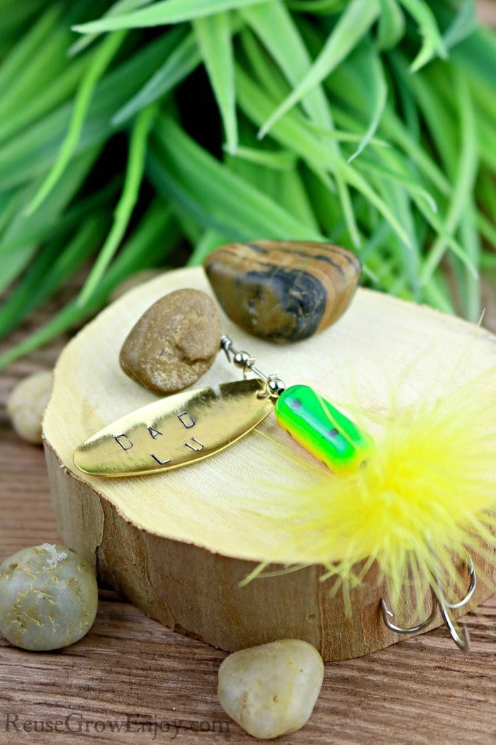 Vibrant fishing lure with green and yellow colors, surrounded by natural stones and green foliage, on a wooden surface for outdoor fishing or tackle display.