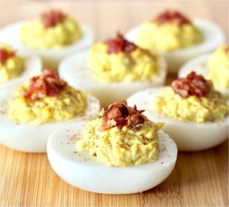 Close-up of deviled eggs topped with crispy bacon bits, served on a wooden surface, highlighting a delicious appetizer for gatherings and parties.