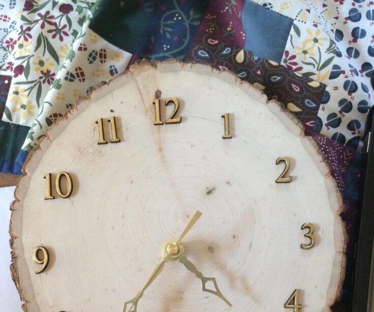 Close-up of a rustic wooden wall clock with gold numbers and hands, mounted on a colorful patchwork quilt background, ideal for farmhouse or vintage interior design.