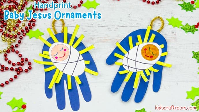 Two colorful Baby Jesus handprint ornaments with smiling faces, yellow and blue paper rays, on a white wooden background with holiday decorations.