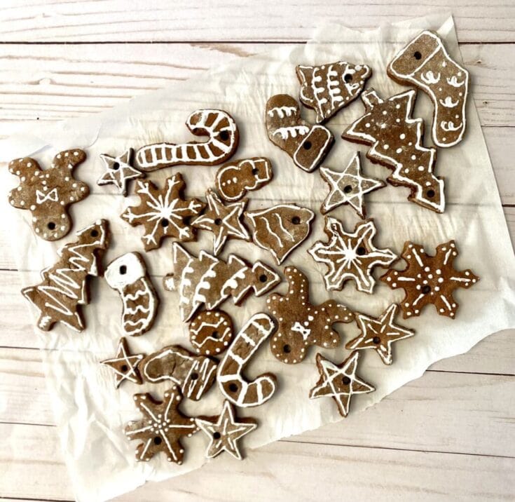 Assorted gingerbread cookies decorated with white icing, shaped like stars, trees, candy canes, and gingerbread men, on white parchment paper for holiday treats.