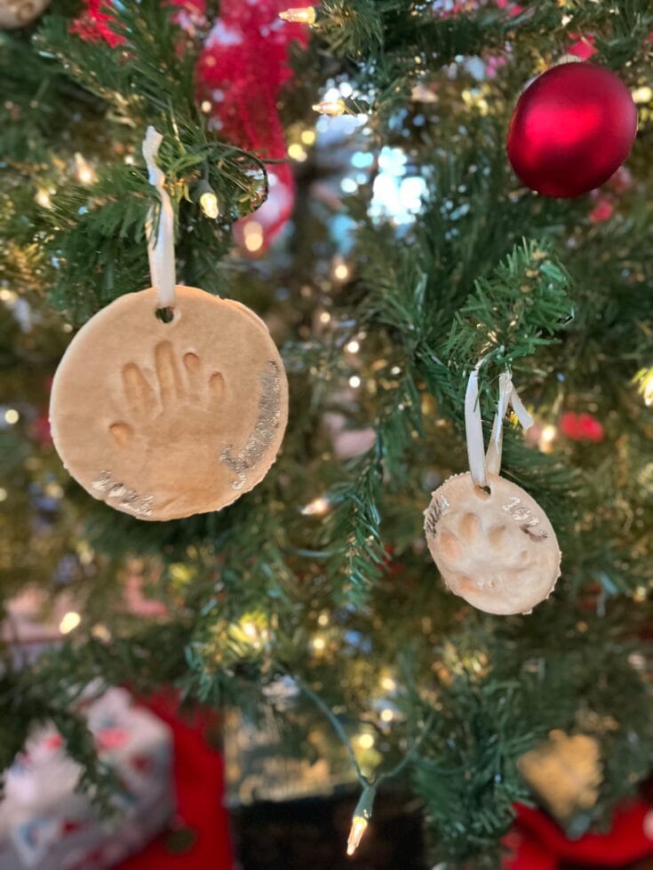 Close-up of handmade cookie ornaments hanging on a decorated Christmas tree with red baubles and warm lights, creating a festive holiday atmosphere.