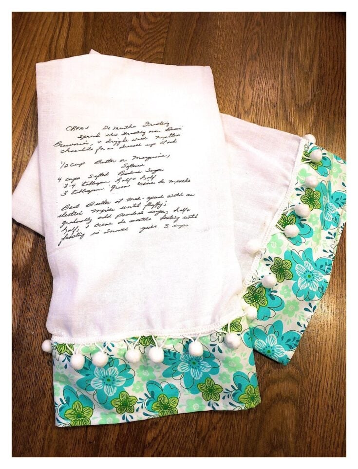 Soft white baby swaddle blanket with colorful blue and green floral trim and pom-pom accents, perfect for newborns and baby photography.