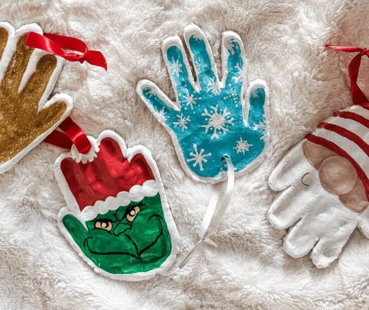Colorful Christmas hand puppets and decorations including a snowflake glove, Santa's elf, and a reindeer, arranged on a soft white surface for holiday celebration.