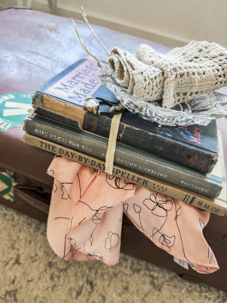 A collection of vintage books, a knitted glove, and a fabric with abstract line art on a table, creating a cozy, artistic scene.